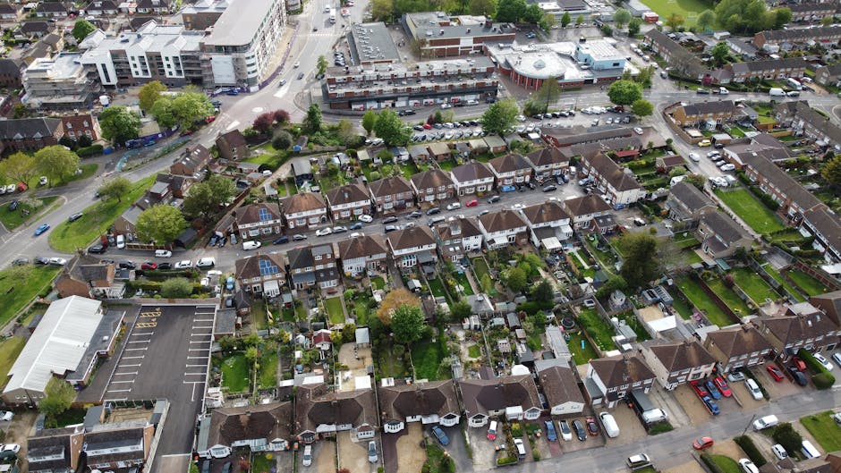 An aerial view of a suburban neighborhood showcasing a variety of back gardens and outdoor spaces. The gardens feature lush green lawns, neatly trimmed hedges, and a mix of trees with dense foliage. M