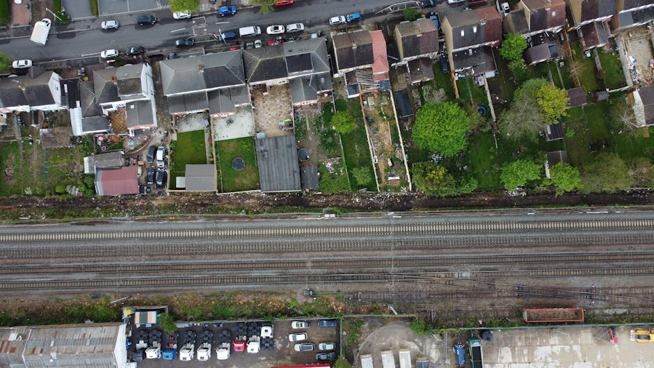 An aerial view of a suburban neighborhood showcasing a variety of back gardens and outdoor spaces. The gardens feature lush green lawns, neatly trimmed hedges, and a mix of trees with dense foliage. M
